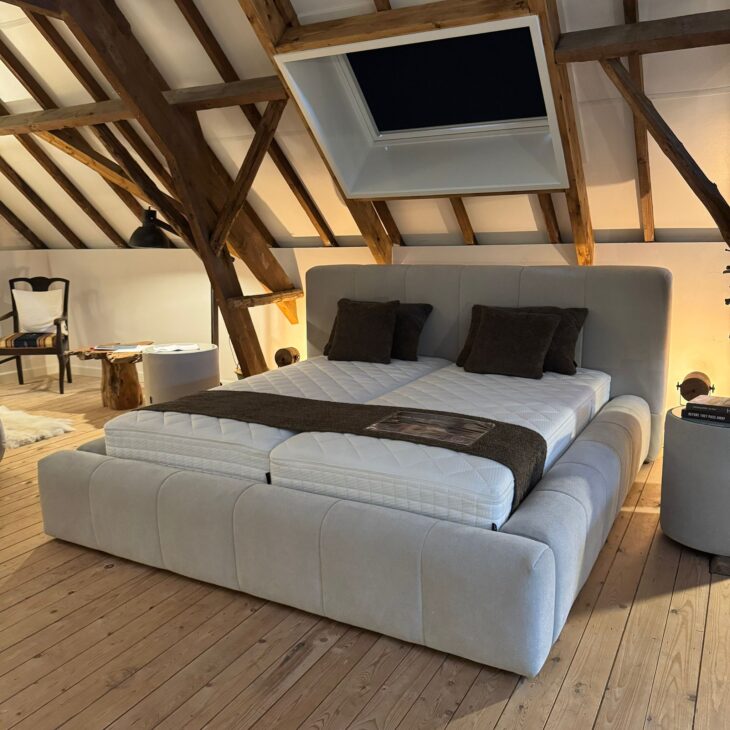 Lichtgrijs gestoffeerd boxspringbed met hoog hoofdbord in een houten zolderslaapkamer