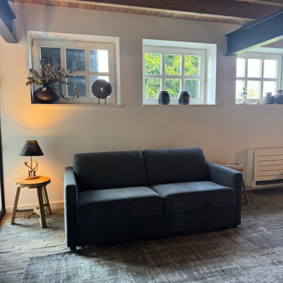 Antracietgrijze tweezits slaapbank in een showroom met balkenplafond