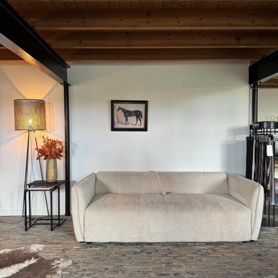 Beige driezitsbank met brede armleuningen onder een houten plafond